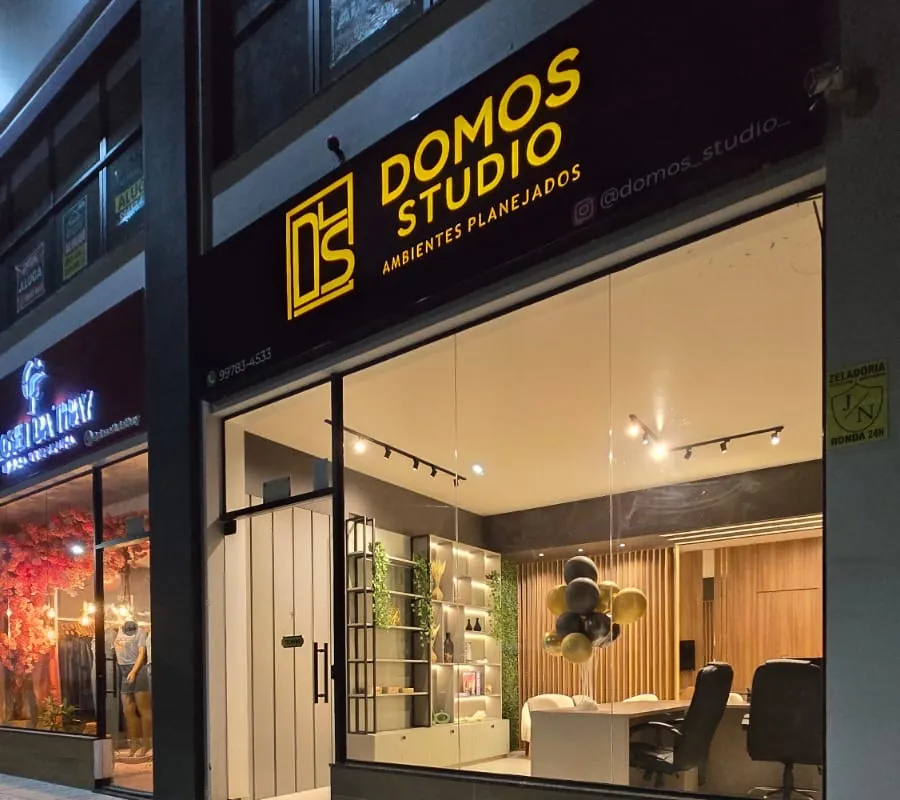 Fachada da Domos Studio à noite, com letreiro iluminado e vitrine do estúdio